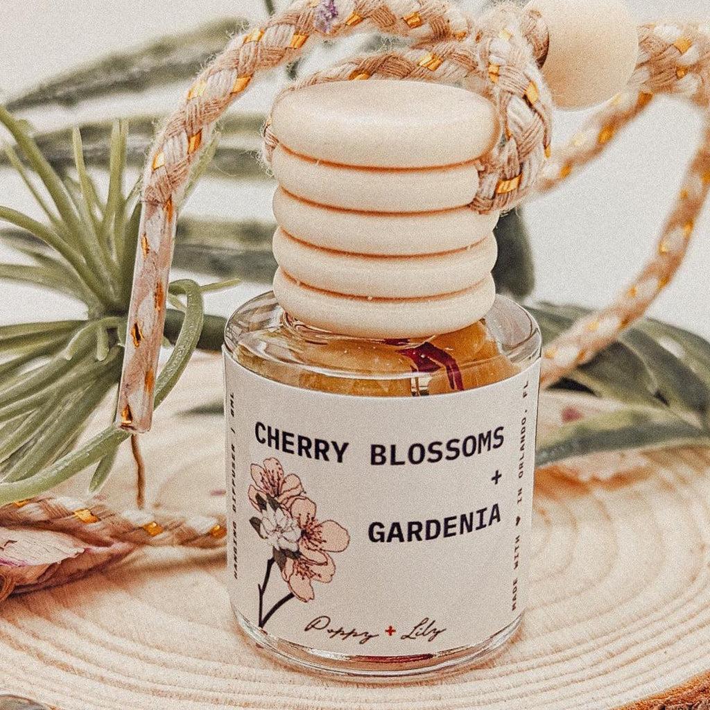 Perfume bottle labeled 'Cherry Blossoms + Gardenia' with decorative elements on a natural background