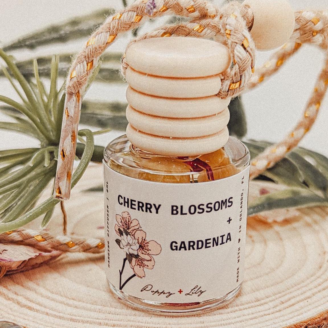 Perfume bottle labeled 'Cherry Blossoms + Gardenia' with decorative elements on a natural background