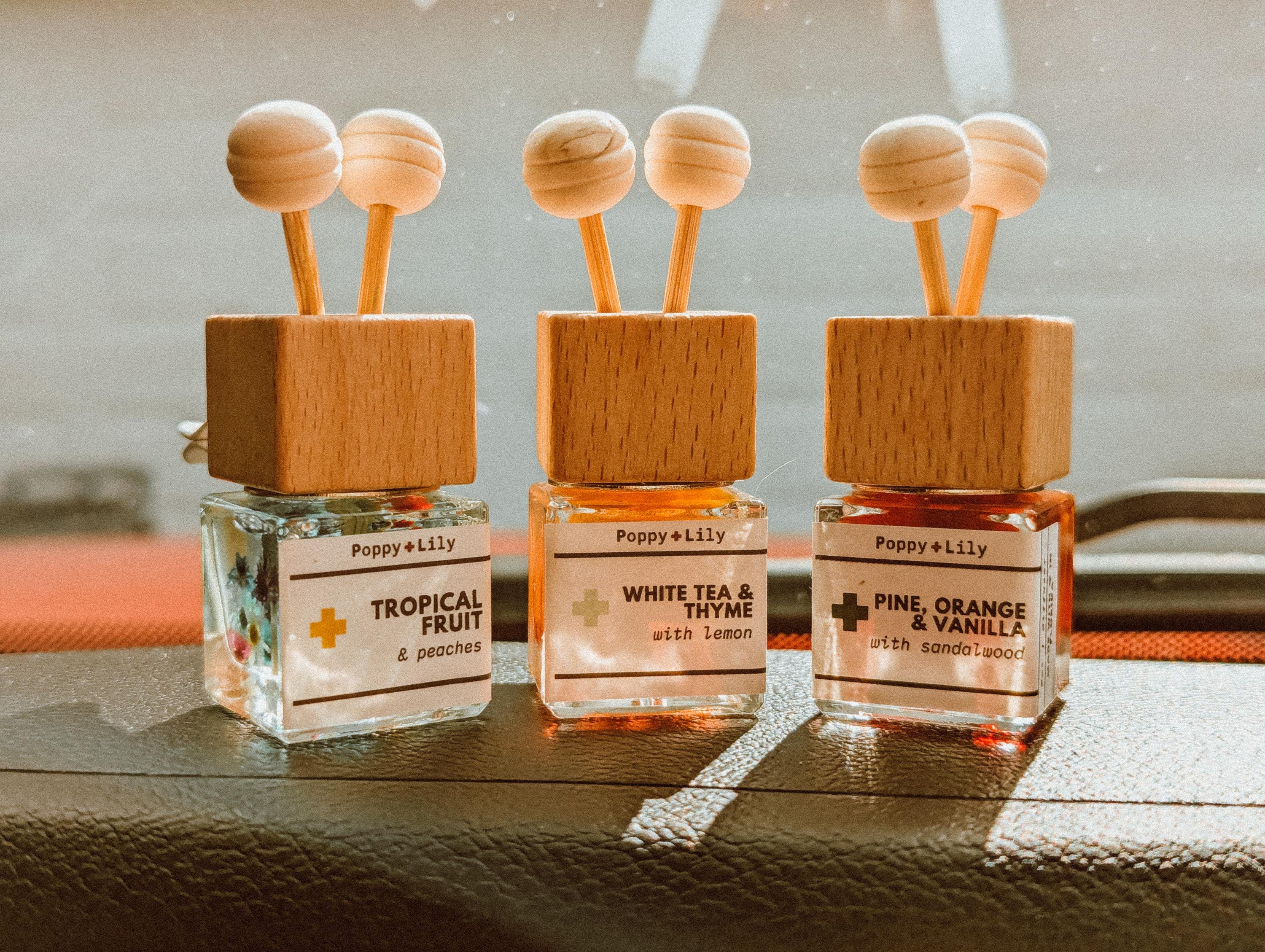Three small bottles of Poppy & Lily diffusers on a wooden surface.