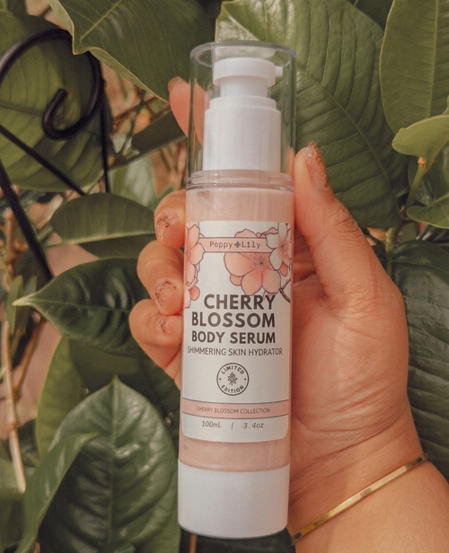 Hand holding a cherry blossom body serum bottle with green leaves in the background