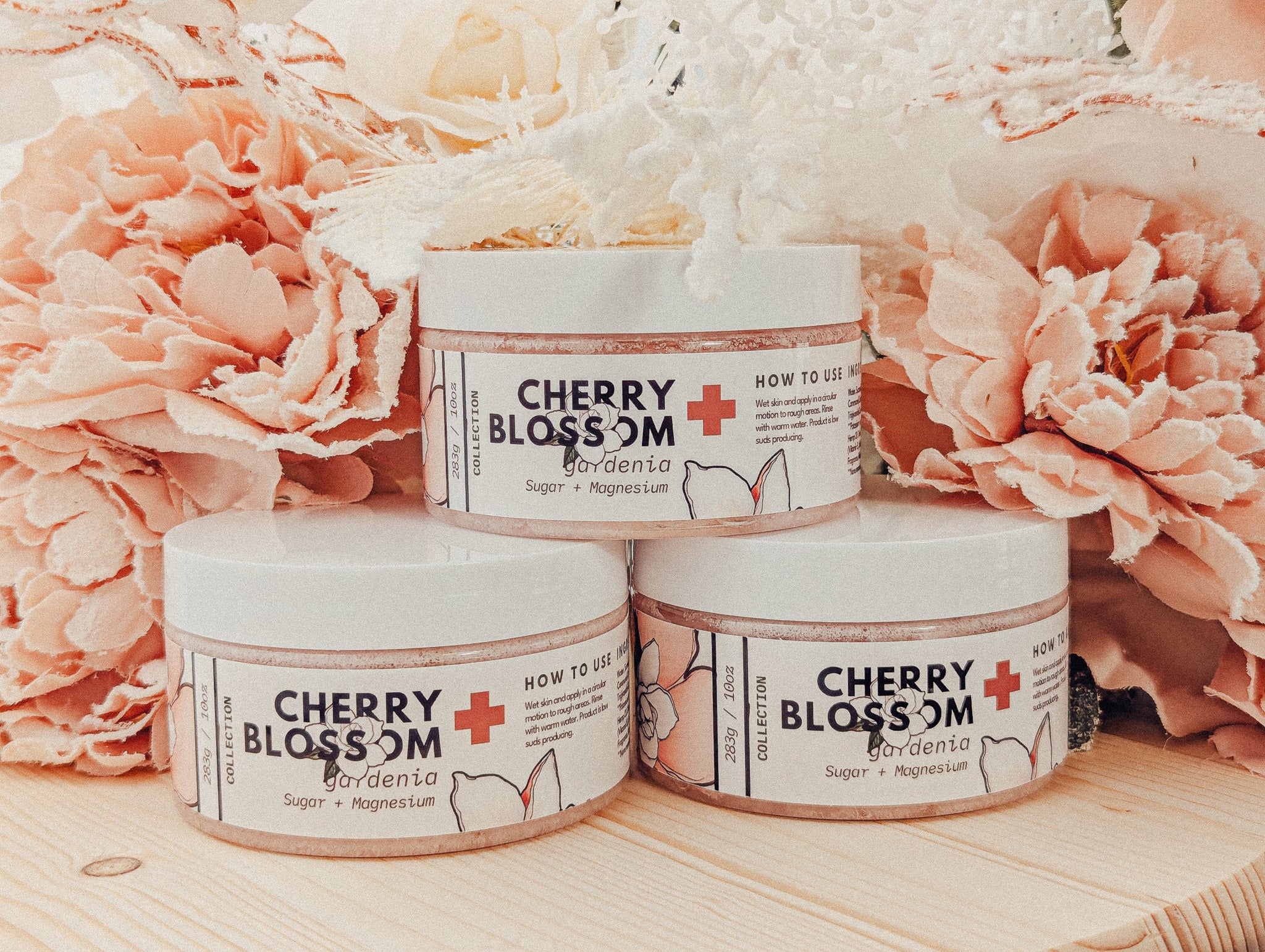 Three Cherry Blossom skincare jars on a wooden surface with pink flowers in the background