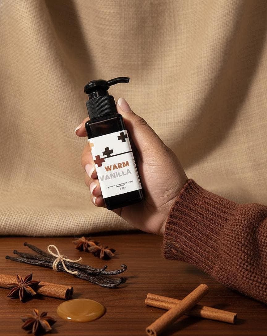 Hand holding a bottle labeled 'Warm Vanilla' with spices on a wooden surface