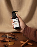 Hand holding a bottle labeled 'Warm Vanilla' with spices on a wooden surface