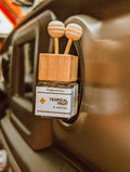 Car air freshener with wooden design and 'Poppy & Lily' label on a car dashboard.