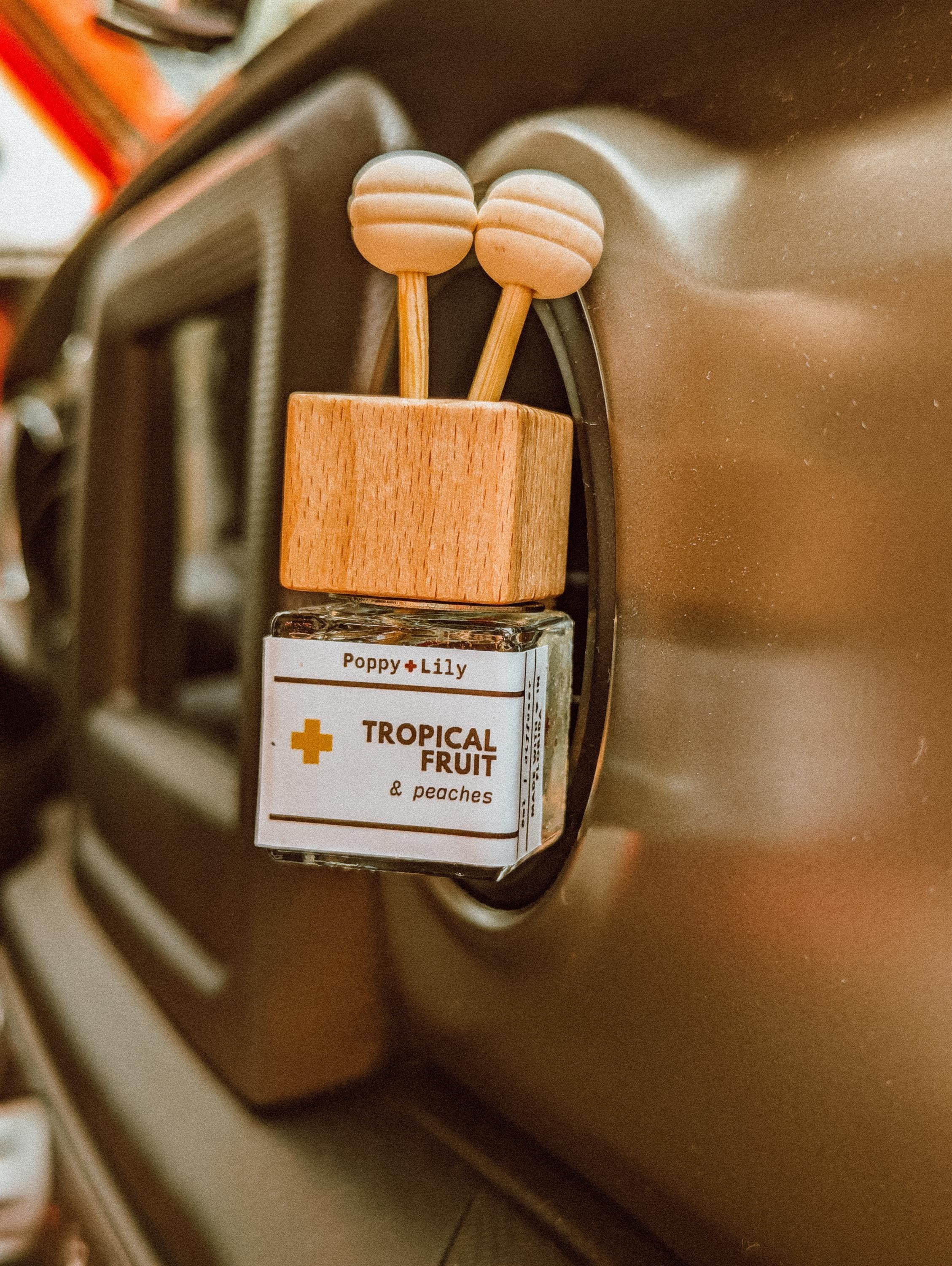 Car air freshener with wooden design and 'Poppy & Lily' label on a car dashboard.