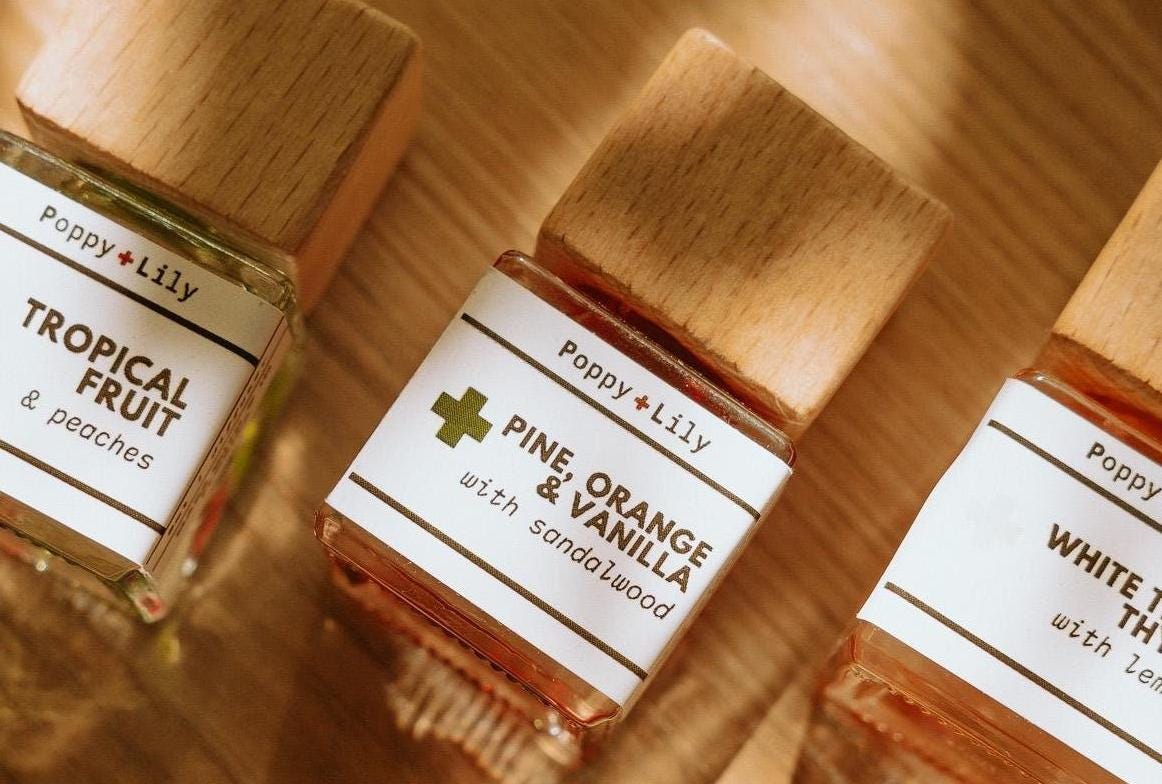 Three small bottles of Poppy & Lily fragrances on a wooden surface.