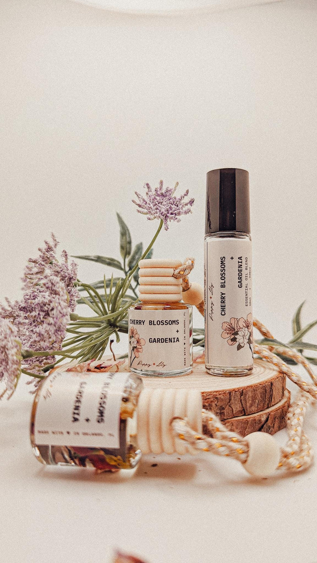 Two small bottles of 'Cherry Blossoms Gardenia' on a wooden block with plants in the background.