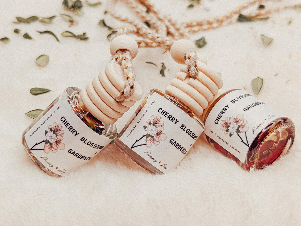 Three Cherry Blossom Gardenia perfume bottles on a light background with floral elements.