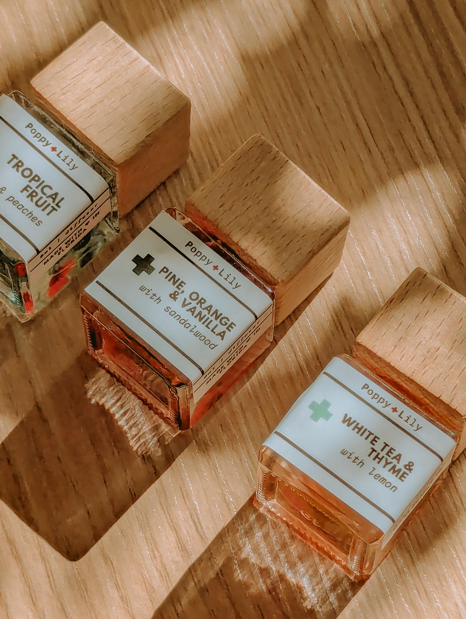 Three small bottles of Poppy & Lily fragrances on a wooden surface