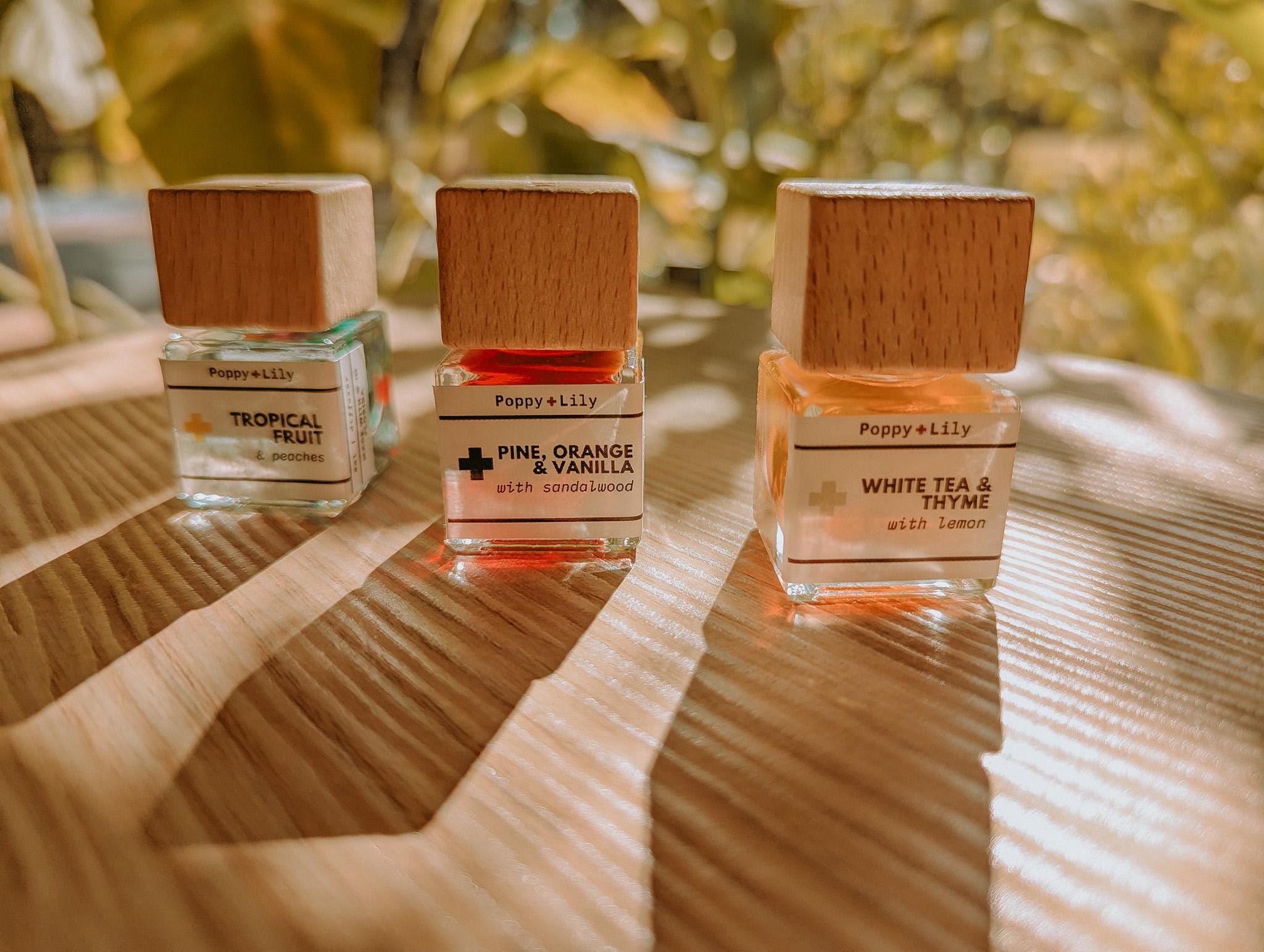 Three perfume bottles by Poppy & Lily on a reflective surface with a blurred natural background