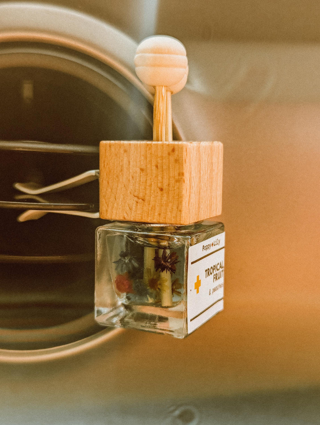 Small glass bottle vent clip diffuser with wooden cap on a metallic surface