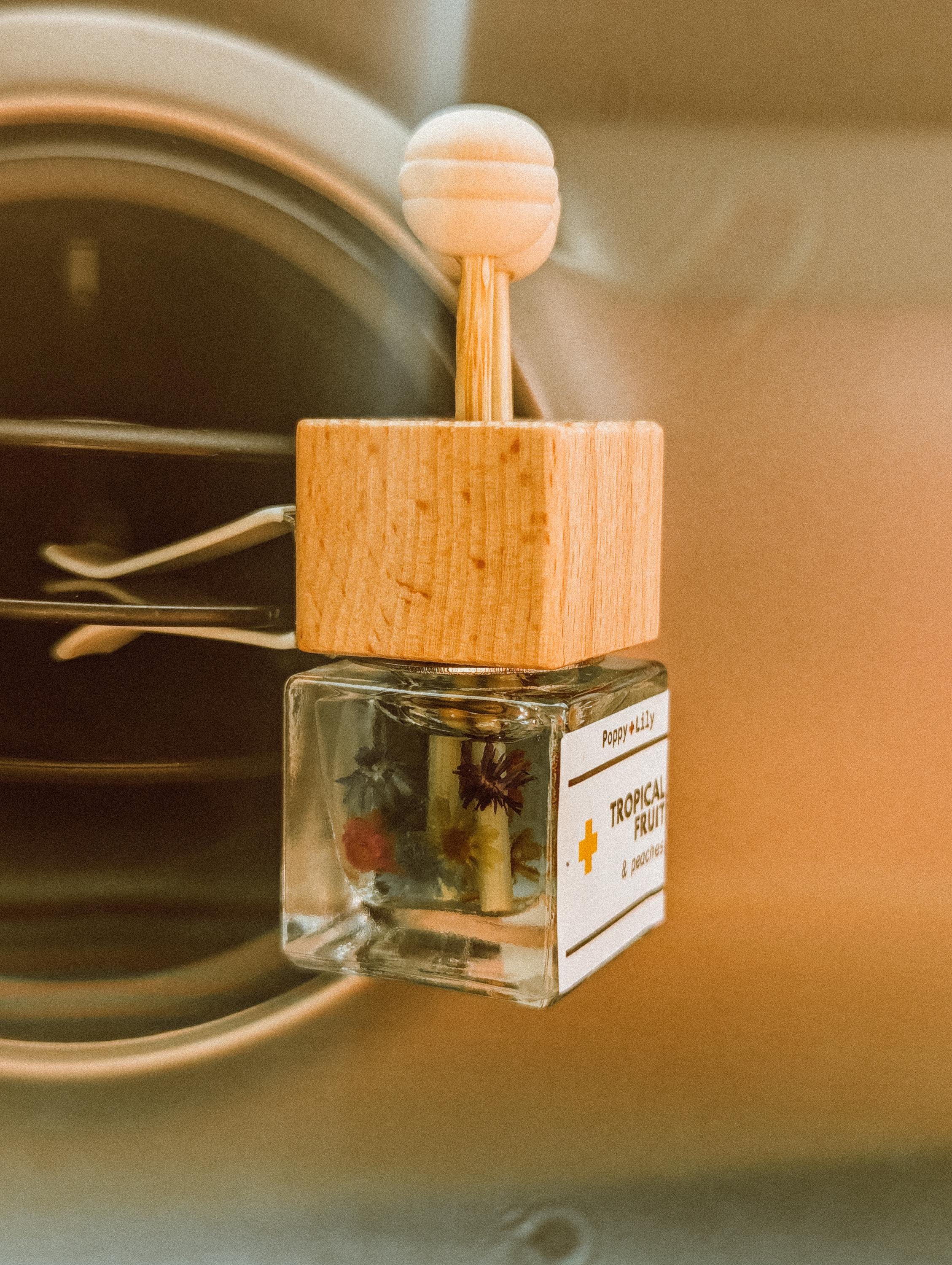 Small glass bottle vent clip diffuser with wooden cap on a metallic surface